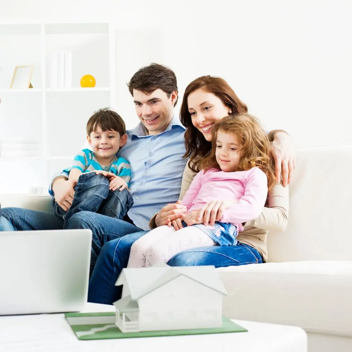 Familia sonriente sentada en un sofá, mirando a una laptop.
