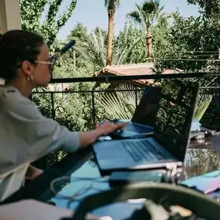 Mujer trabajando en una computadora portátil al aire libre, rodeada de vegetación.