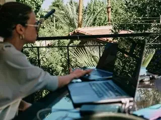 Mujer trabajando en un portátil al aire libre, rodeada de vegetación.
