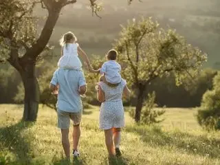 Familia caminando por un campo, con un niño en los hombros y una niña de pie.