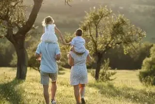 Familia caminando por un campo al atardecer, con un niño en hombros.