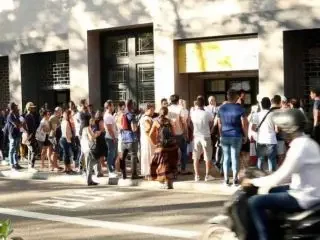 Multitud de personas haciendo fila frente a un edificio en una calle urbana.