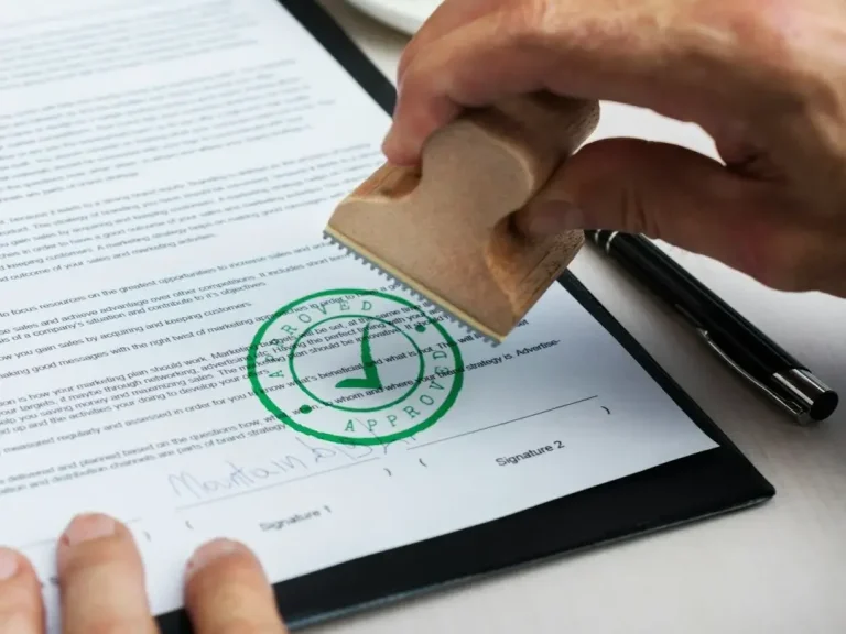 Una mano coloca un sello verde sobre un documento con un tick y texto impreso.