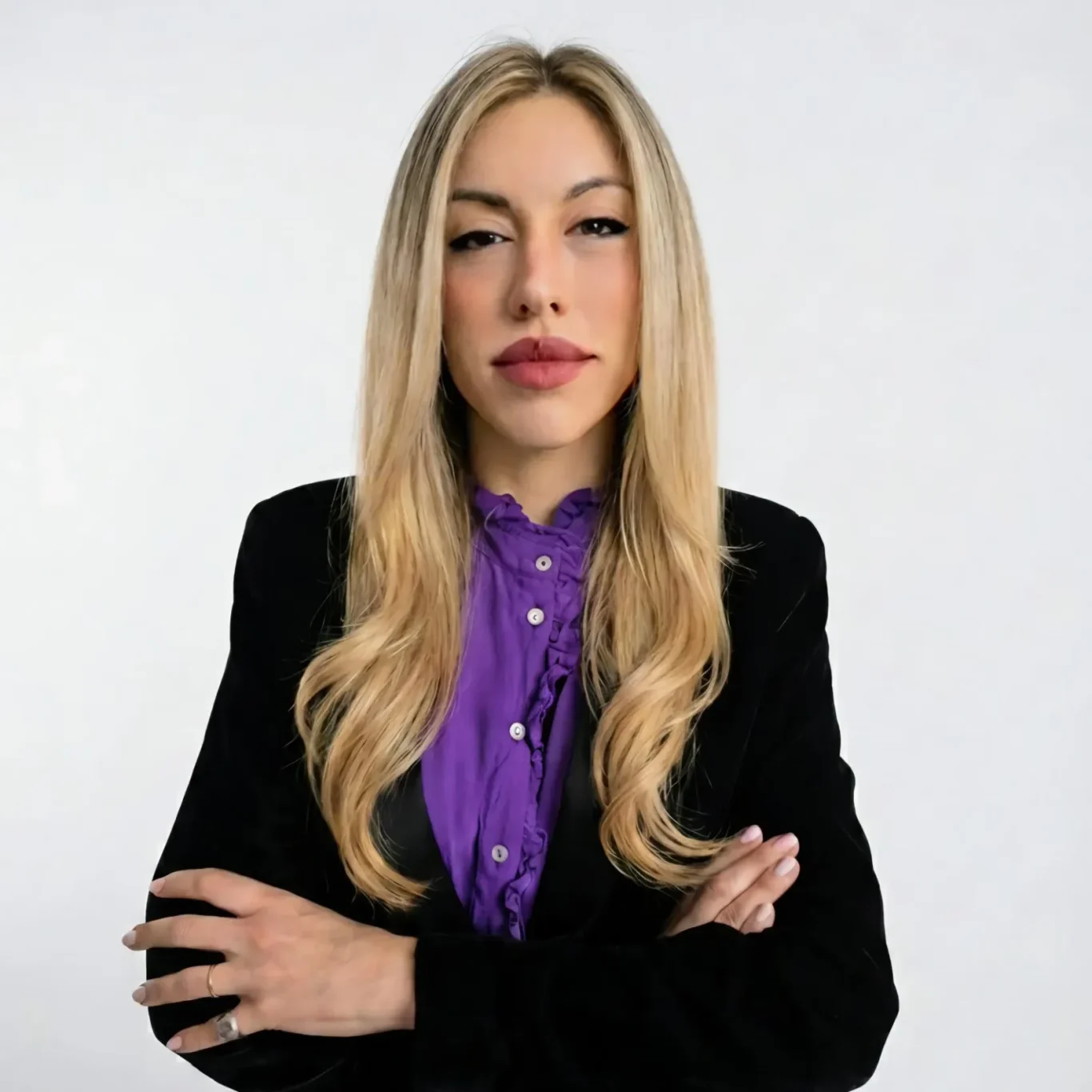 Mujer de cabello largo y lacio, viste un blazer negro y camisa morada, con brazos cruzados.