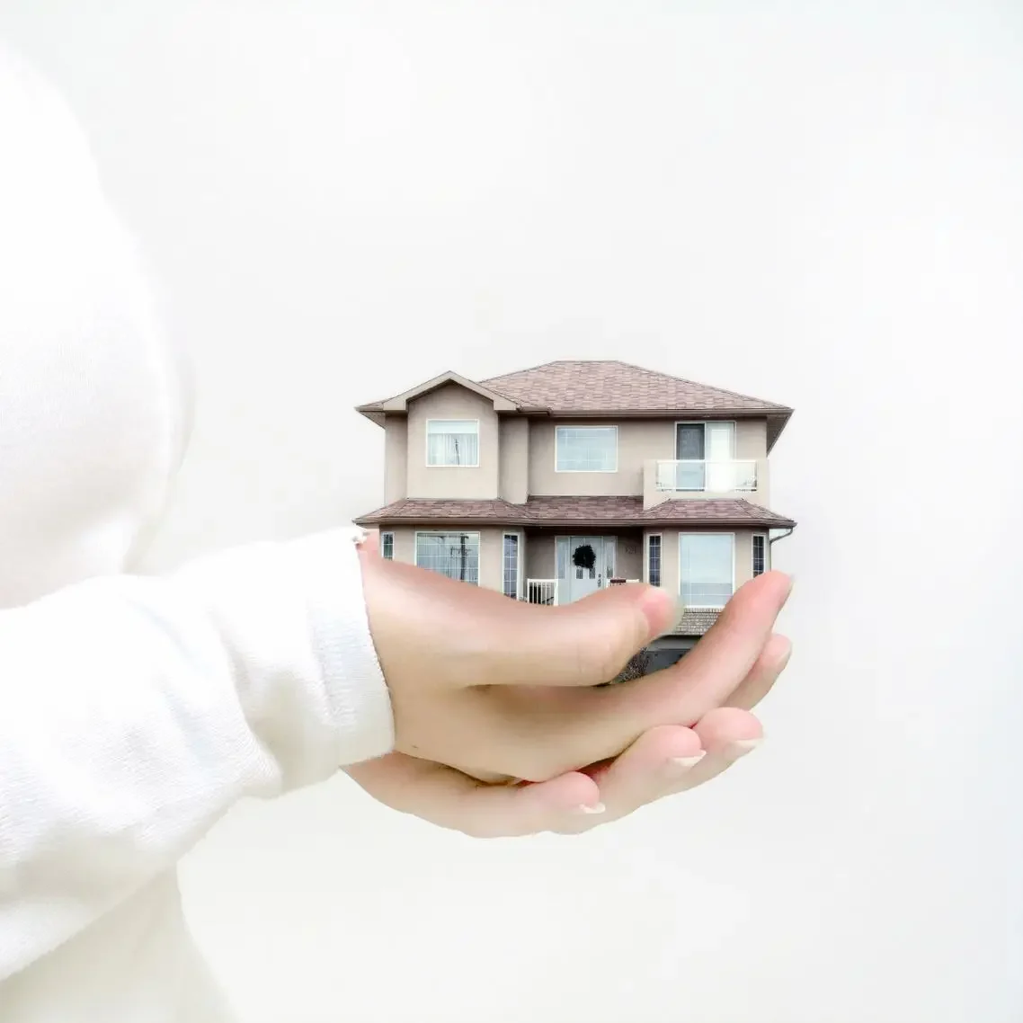 Casa pequeña sostenida en una mano, sobre fondo blanco.